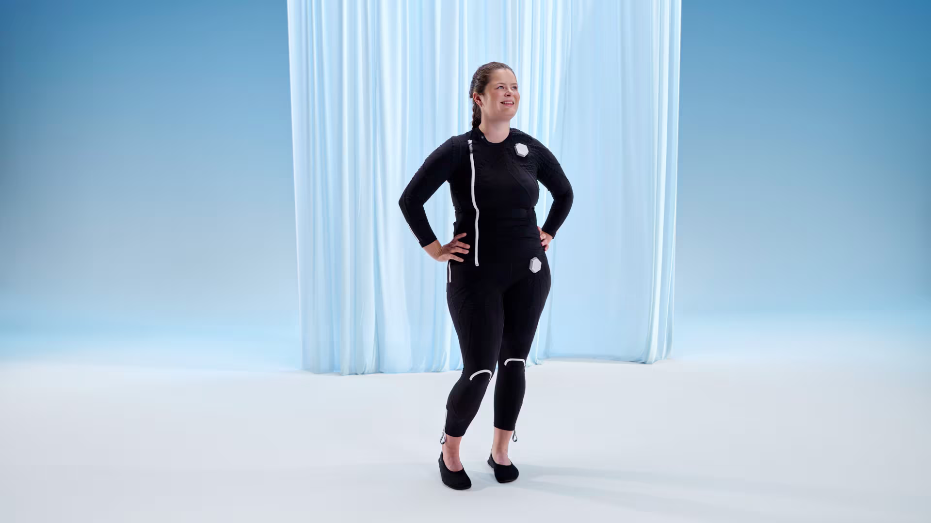 Auf dem Bild sieht man eine lächelnde junge Frau die den exopulse suit trägt. 