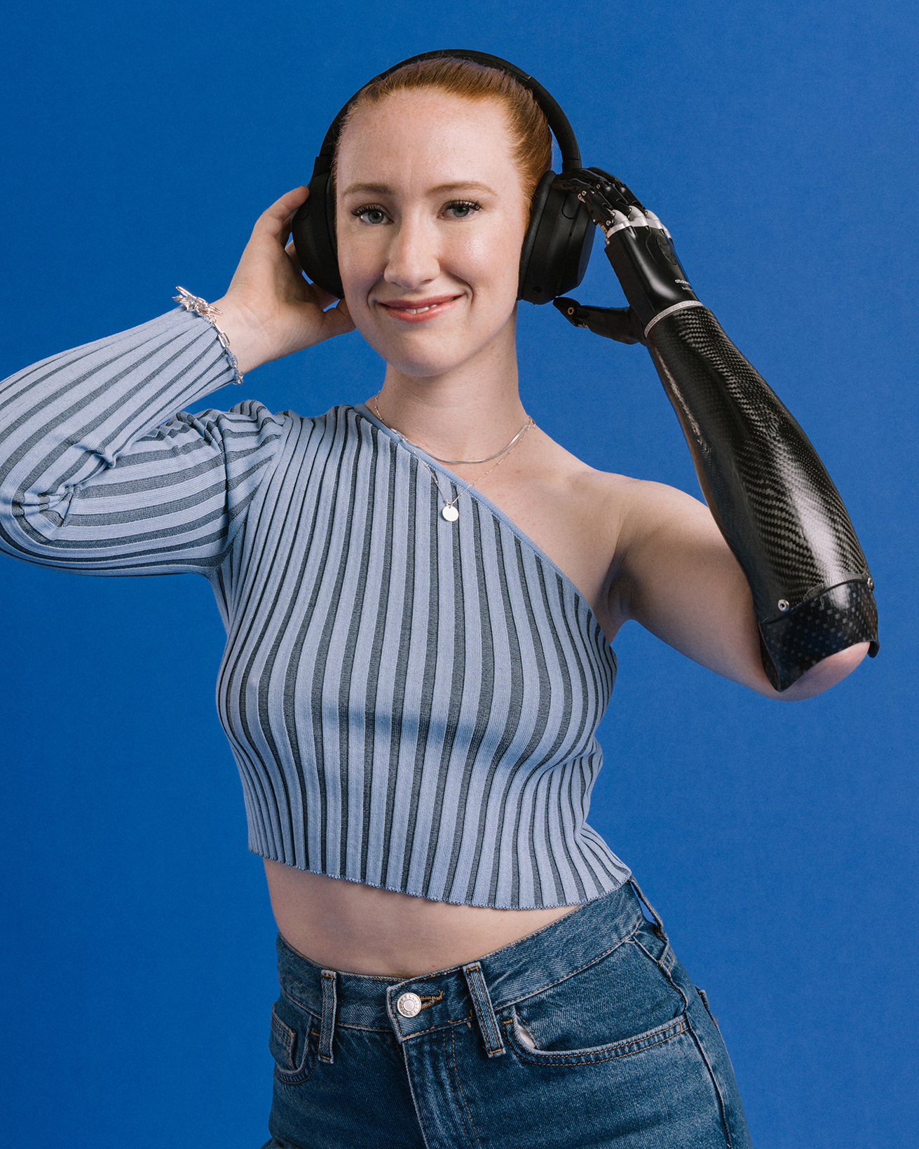 Prosthetic arm user Enya with Ottobock bebionic hand listening to music, holding her headphones.