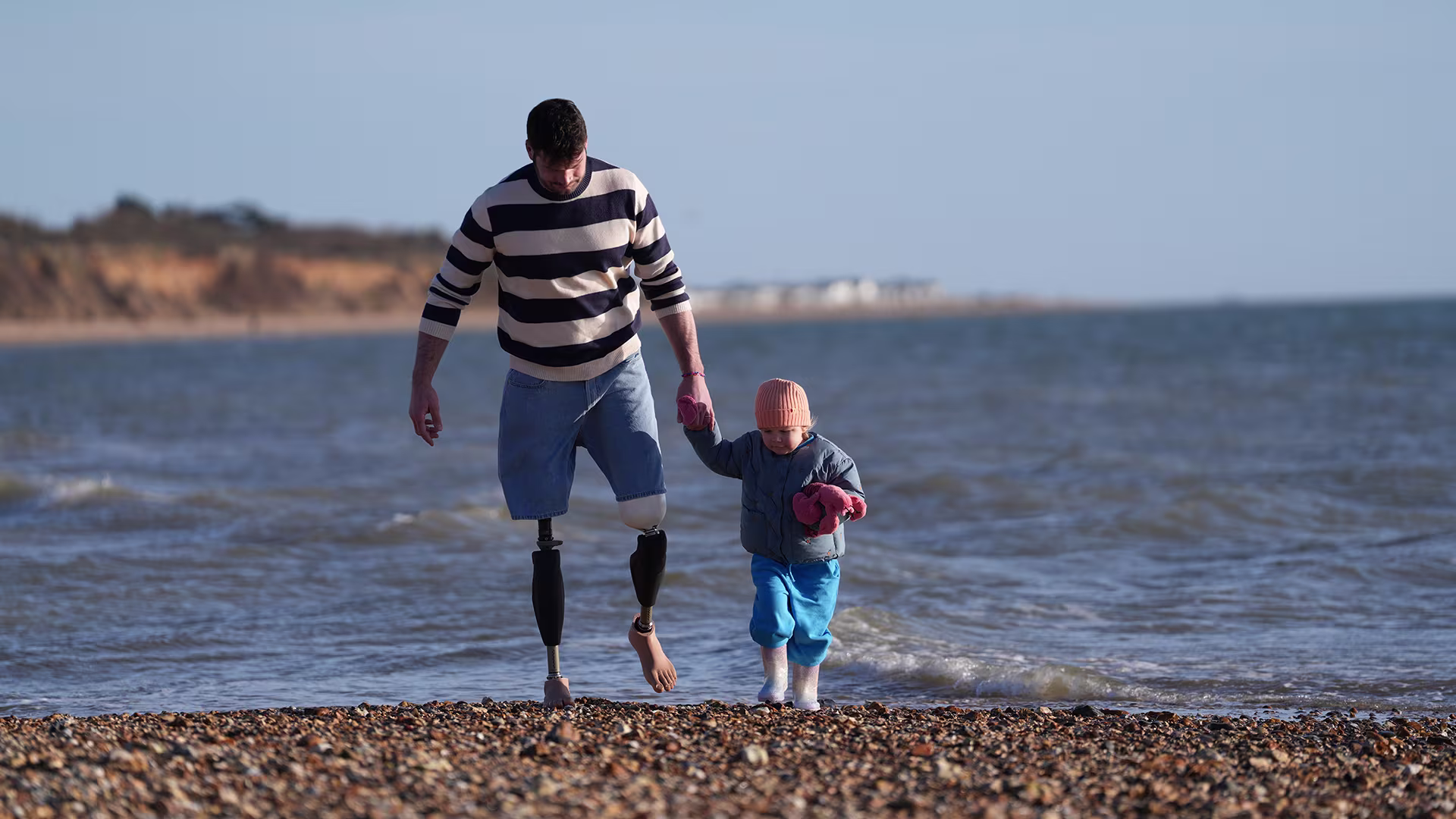 A bilateral amputee wearing Ottobock Genium X4 walking on the beach with his daughter.