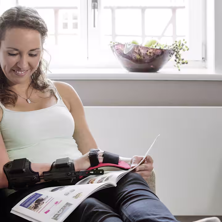 A woman sitting on a sofa reading a magazine wearing a hand orthosis from Ottobock.