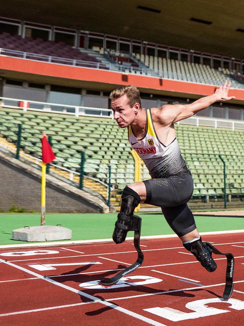 A bilateral amputee races to the finish line of a track field, sporting Ottobock's Runner prosthetic feet