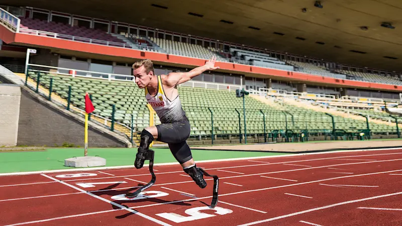 A bilateral amputee races to the finish line of a track field, sporting Ottobock's Runner prosthetic feet