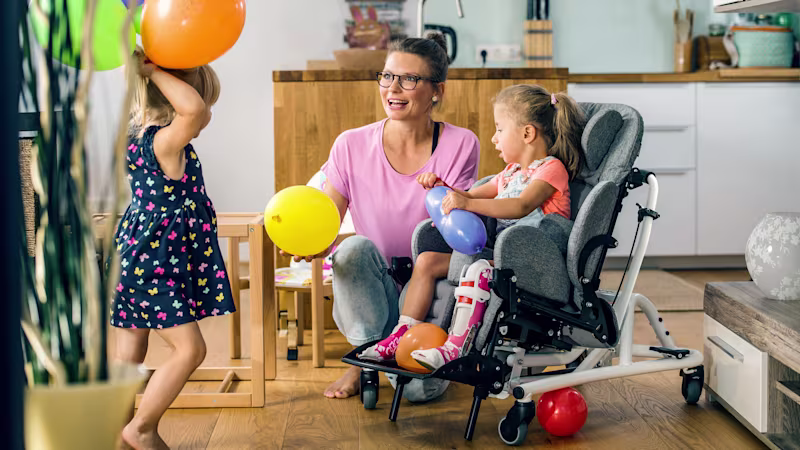 Emilia sitzt in einem Kimba Home und spielt mit ihrer Schwester und Mutter mit Luftballons