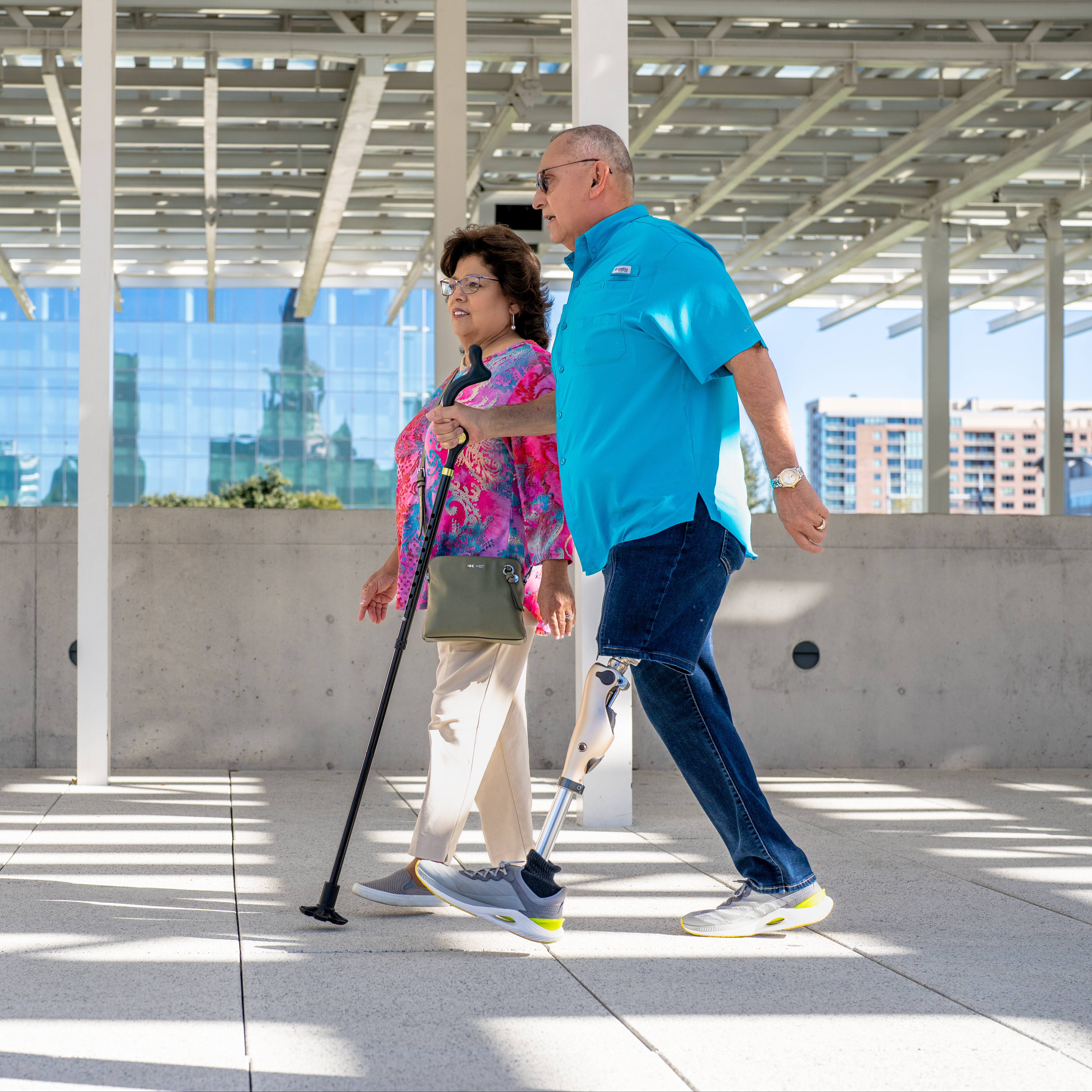 An elder artificial leg user walking through a parking garage with a companion