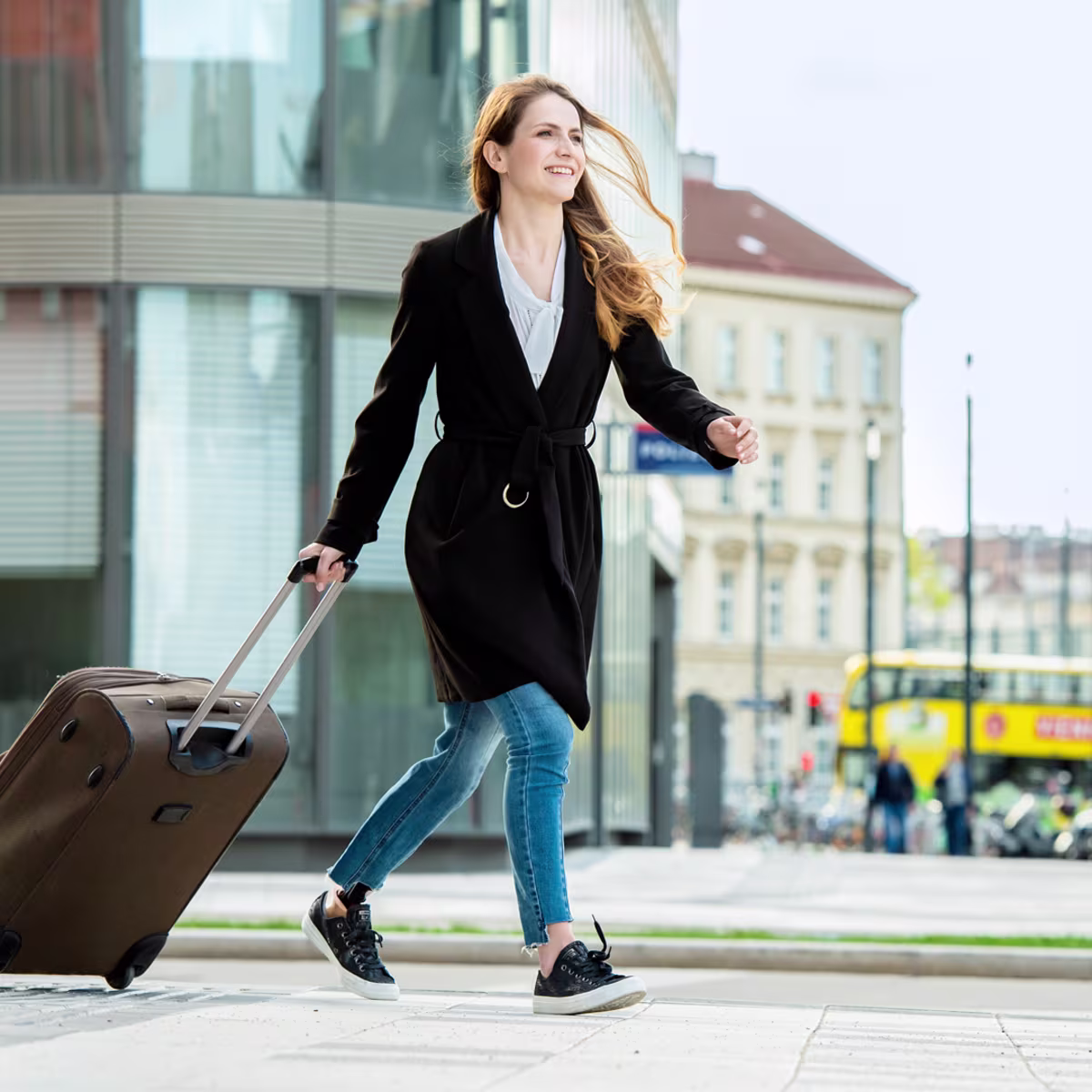 Young woman with Ottobock prosthetic leg in a city smiling as she pulls a wheeled suitcase behind her