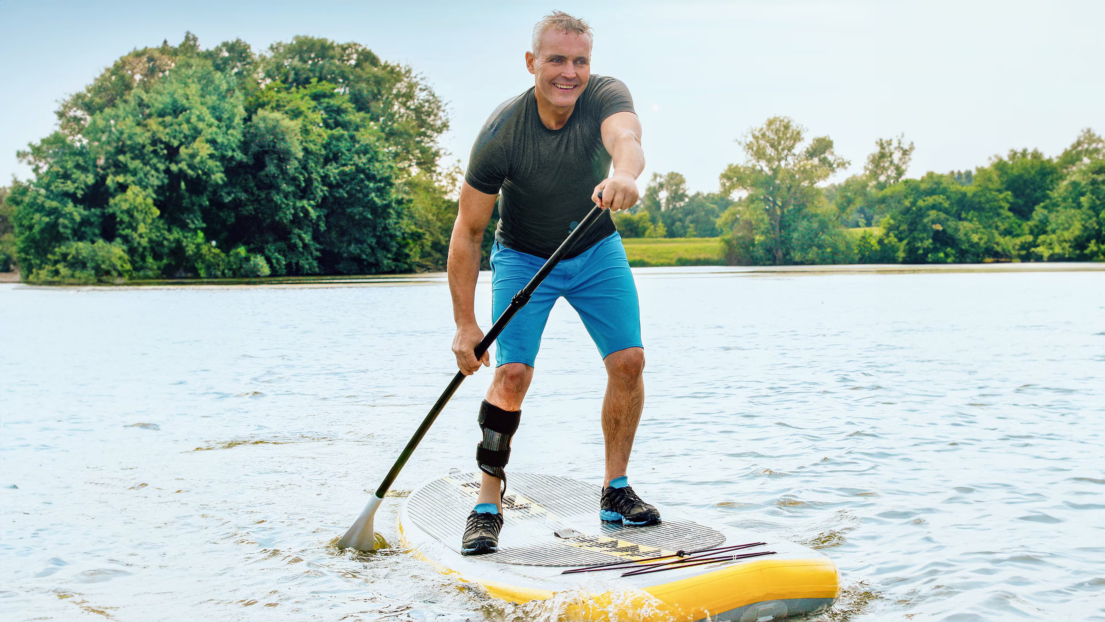 A man with an orthosis paddles across a lake on a SUP.
