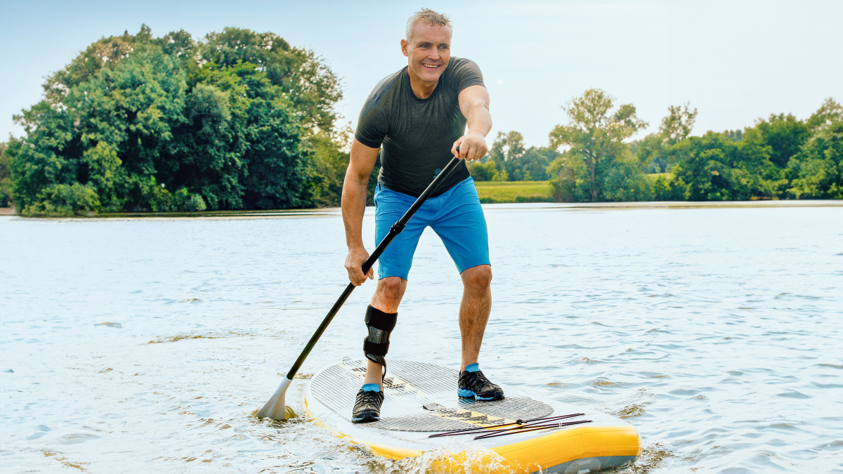 Ein Mann mit Orthese paddelt mit einem SUP über einen See.