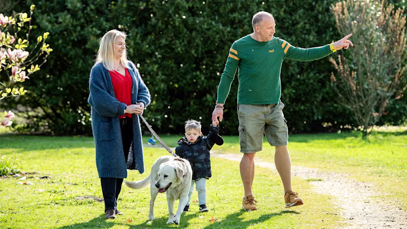 Auf dem Bild sieht man eine Familie mit Mutter, Vater, Kind und Hund. Sie gehen draußen spazieren, der Vater trägt eine farbige Beinprothese, das Genium Kniegelenk.