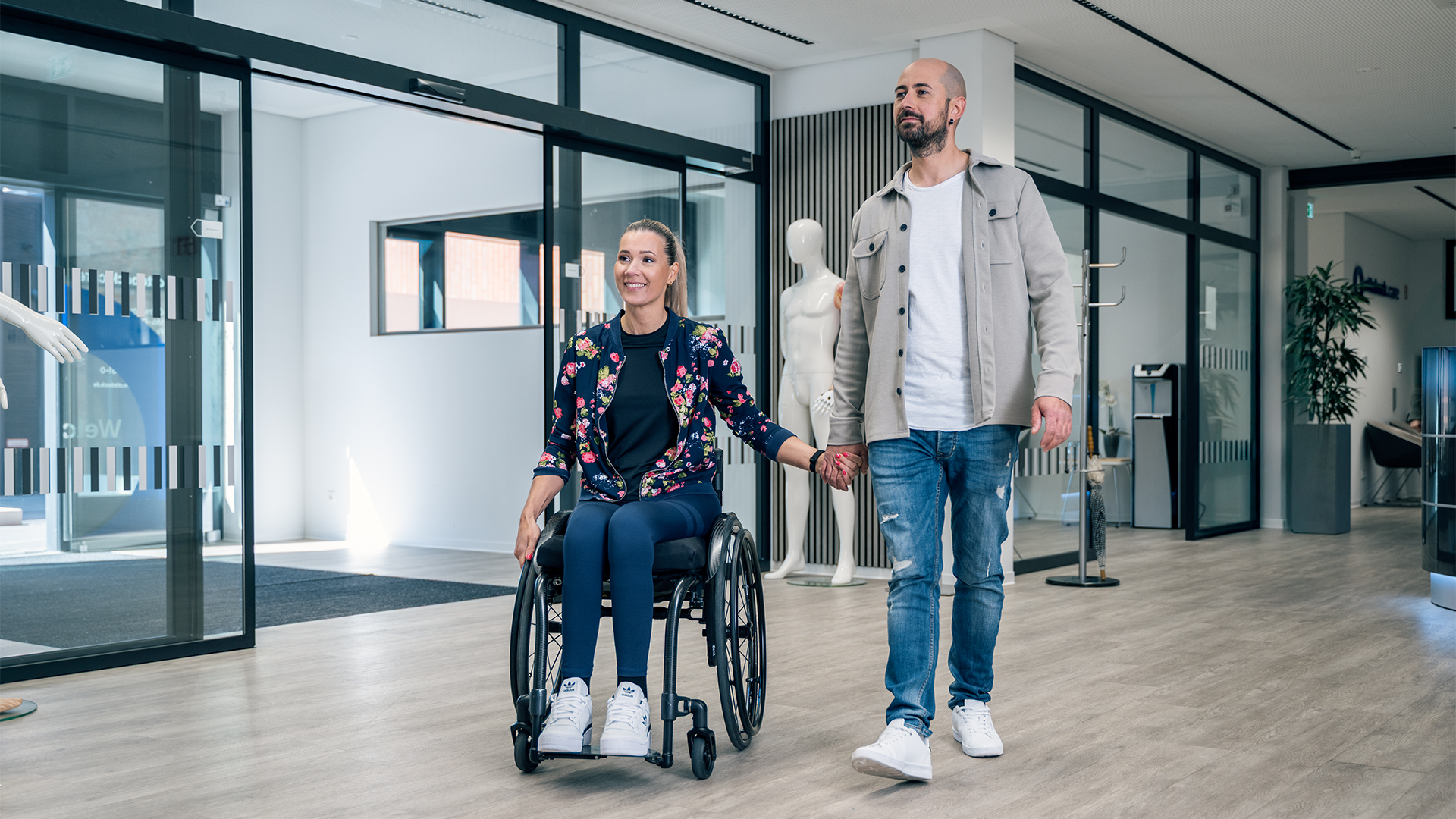 Ein Patient im Rollstuhl lächelt und hält Hände mit dem Mann neben ihr