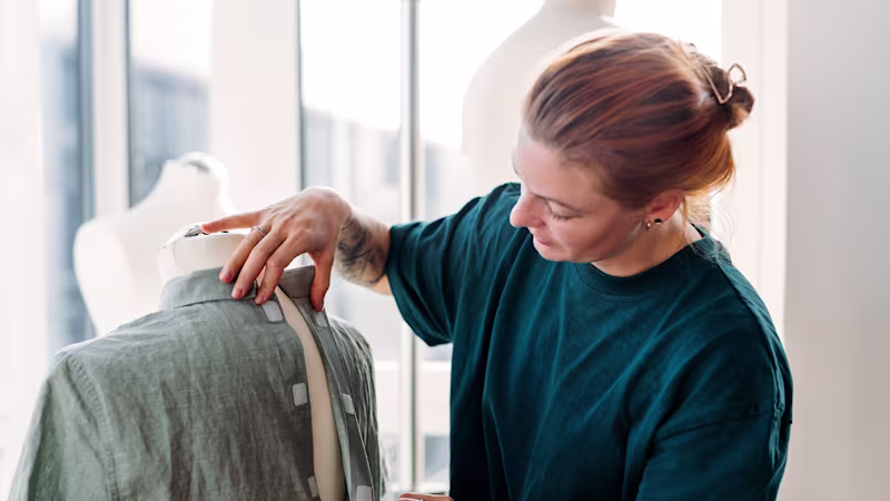 Una stilista di Zalando sistema un capo verde su un manichino fissando la chiusura posteriore con strisce di velcro in uno studio illuminato.
