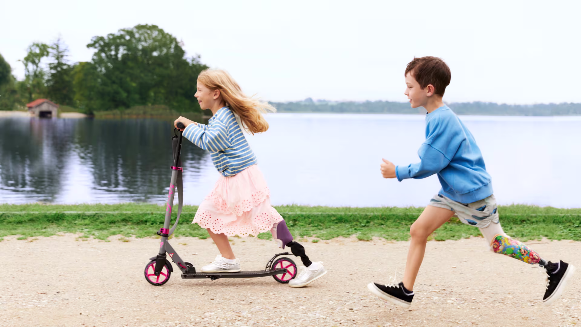 Auf dem Bild sieht man ein junges Mädchen und einen Jungen, auf einem Roller und hinterher laufend. Die beiden Kinder tragen die Beinprothesen Maverick junior & movido.