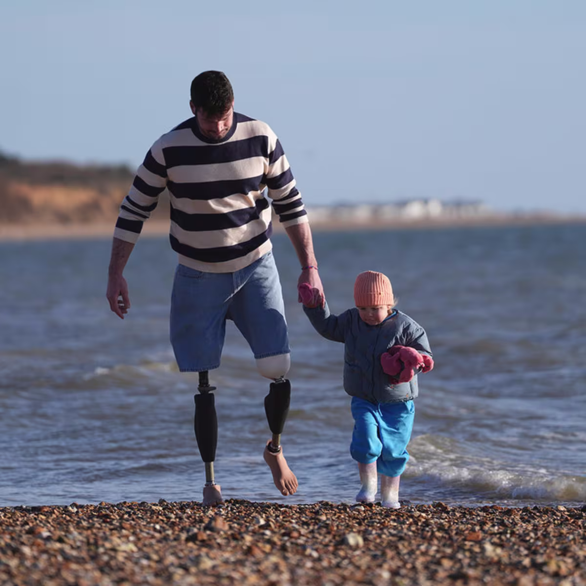 Ein bilateral amputierter Mann geht mit seiner Tochter am Strand spazieren und trägt an beiden beiden das mechatronische Prothesenkniegelenk Genium X4 von Ottobock.