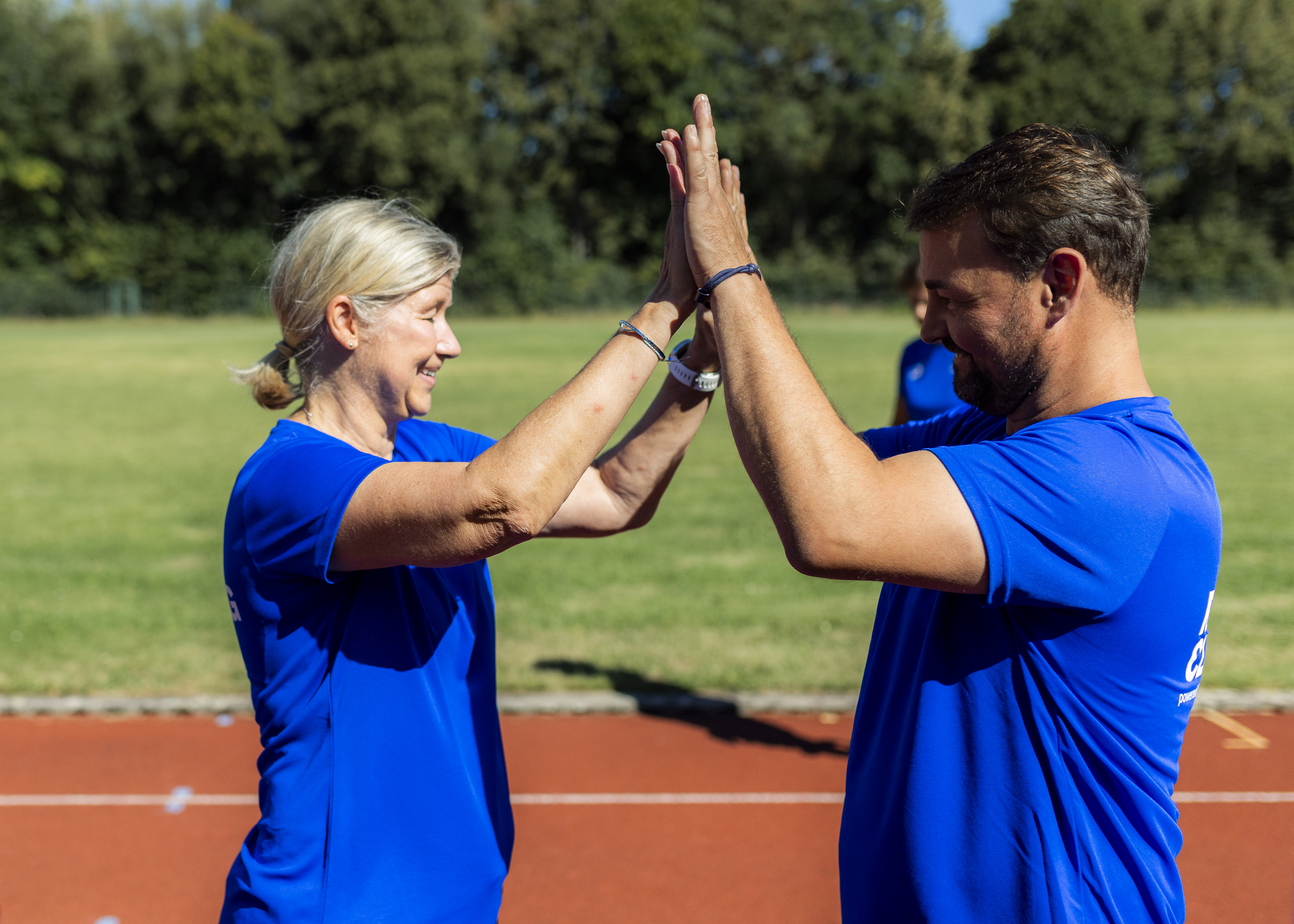 Two runners in blue shirts high-fiving on a running track during Ottobock event