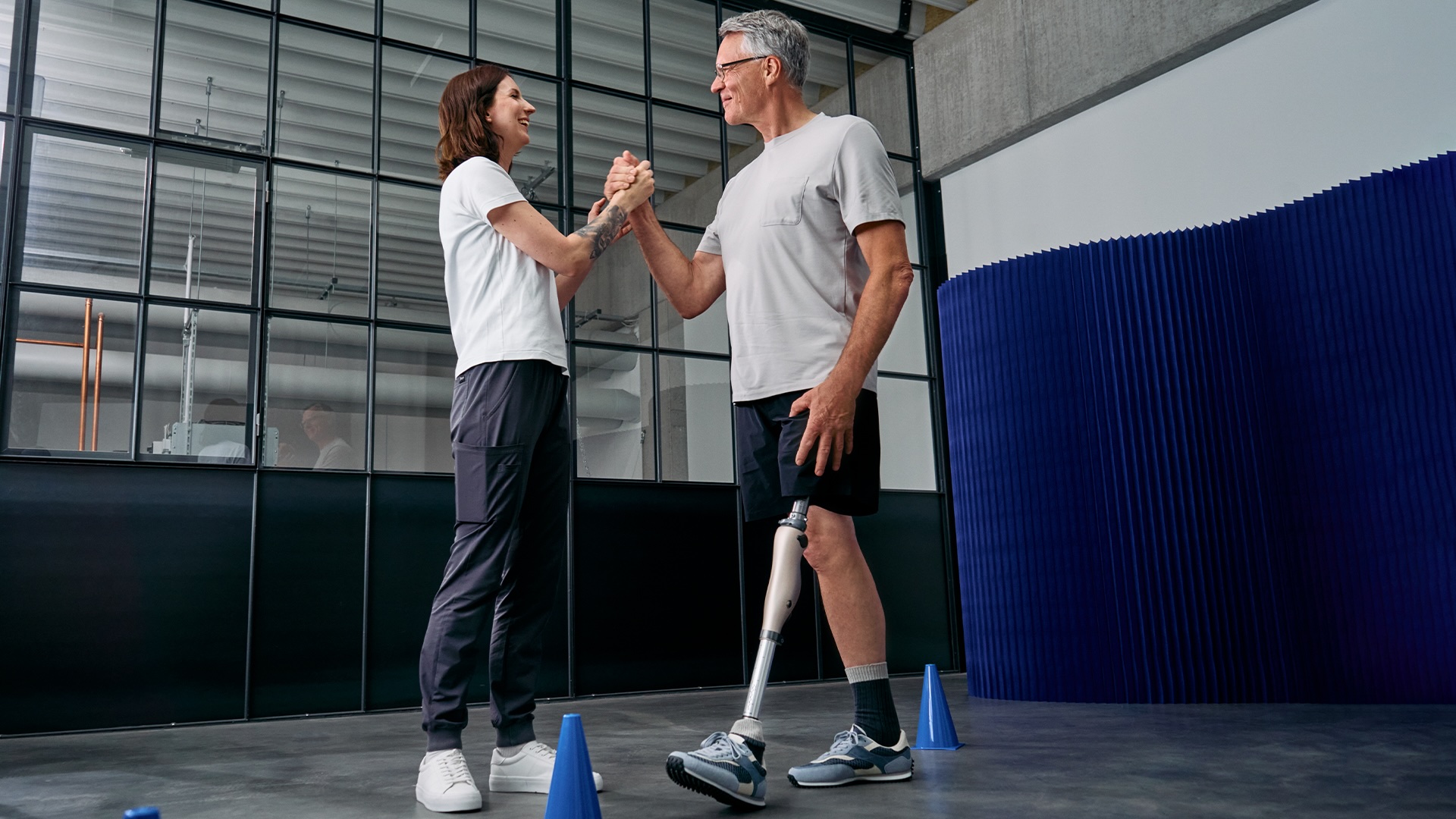 Ein amputierter Mann trägt das mechatronische Kniegelenk Kenevo von Ottobock. Er und seine Therapeutin schlagen zu einem High-Five ein.