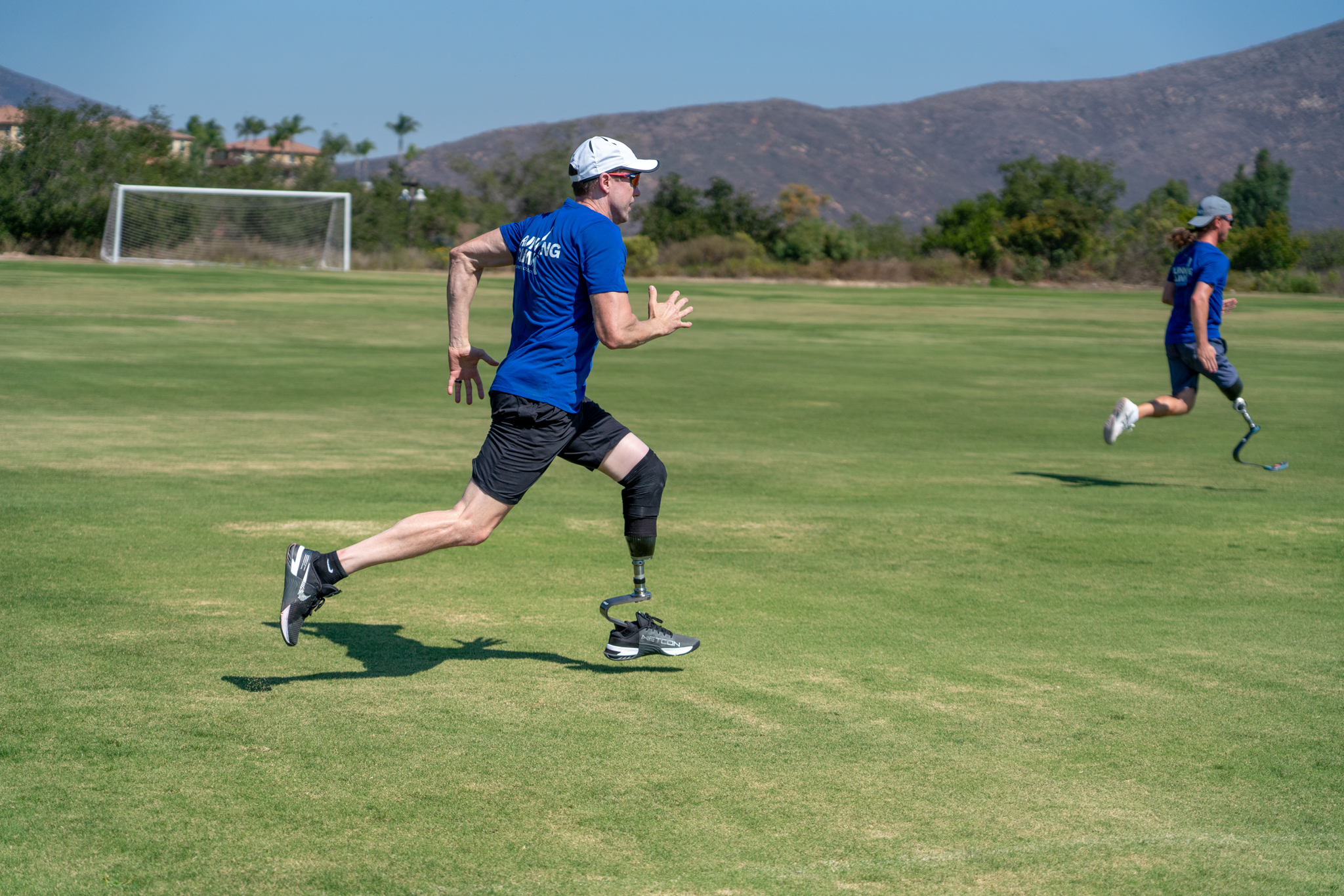 An amputee running across a grass field with other Ottobock Running Clinic participants