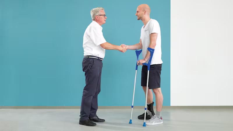 Ein Anwender und ein Orthopäde verabschieden sich nach einer erfolgreichen Therapiestunde. Der Anwender hat einen Fersenbeinbruch erlitten und trägt die FEO Fersenentlastungsorthese von Ottobock.