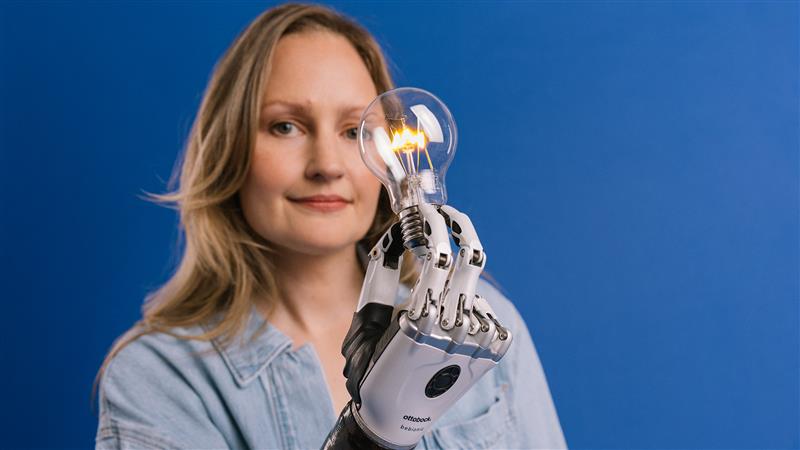 A woman with a bebionic prosthetic hand holding a light bulb. 