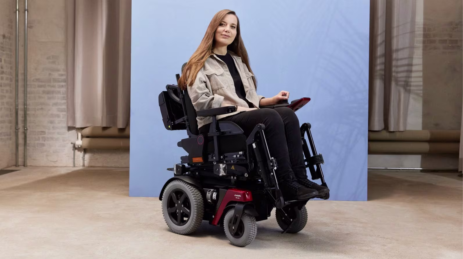 Power wheelchair user Kristina is in Ottobock Juvo B4, in front of a blue photo studio background.
