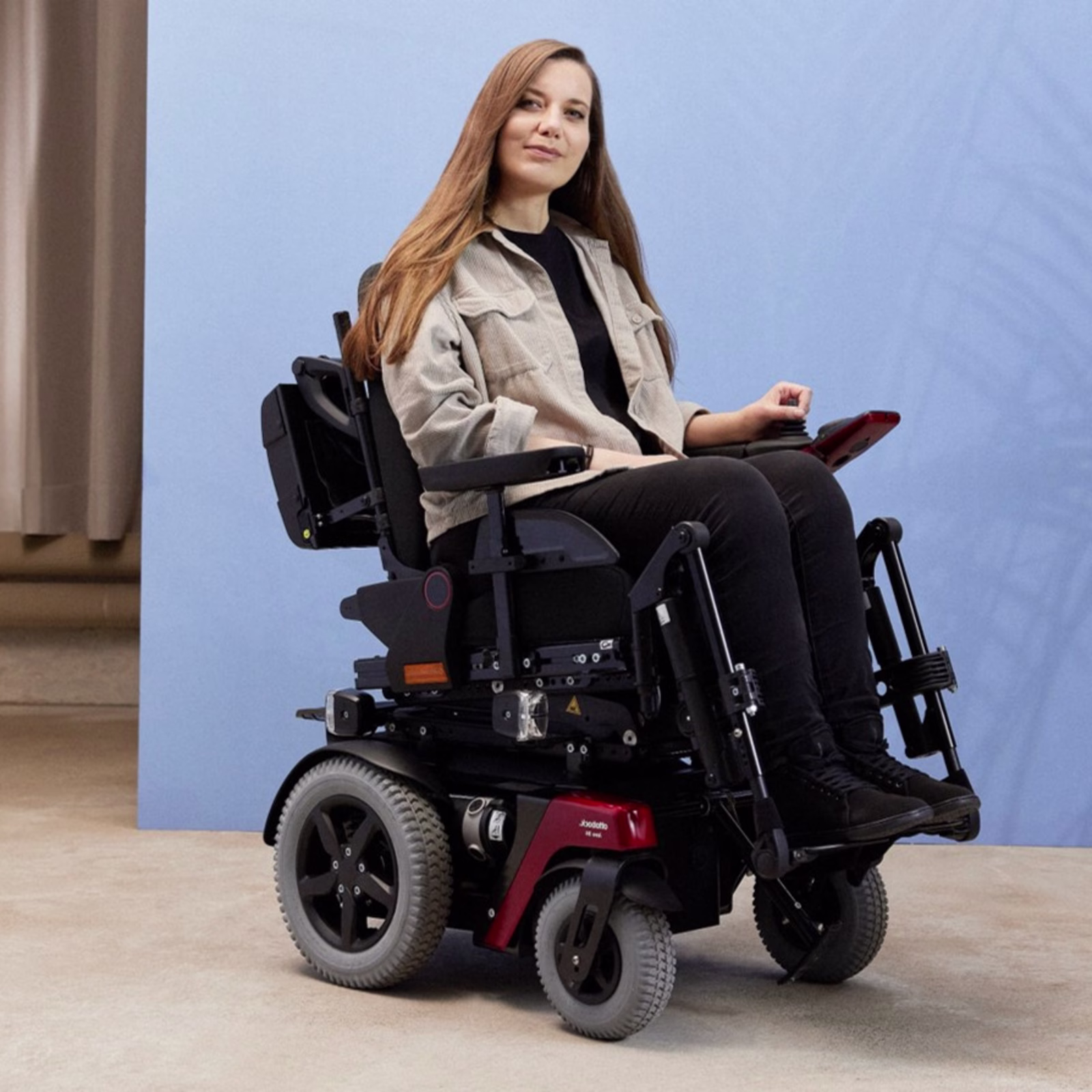 Power wheelchair user Kristina is in Ottobock Juvo B4, in front of a blue photo studio background.
