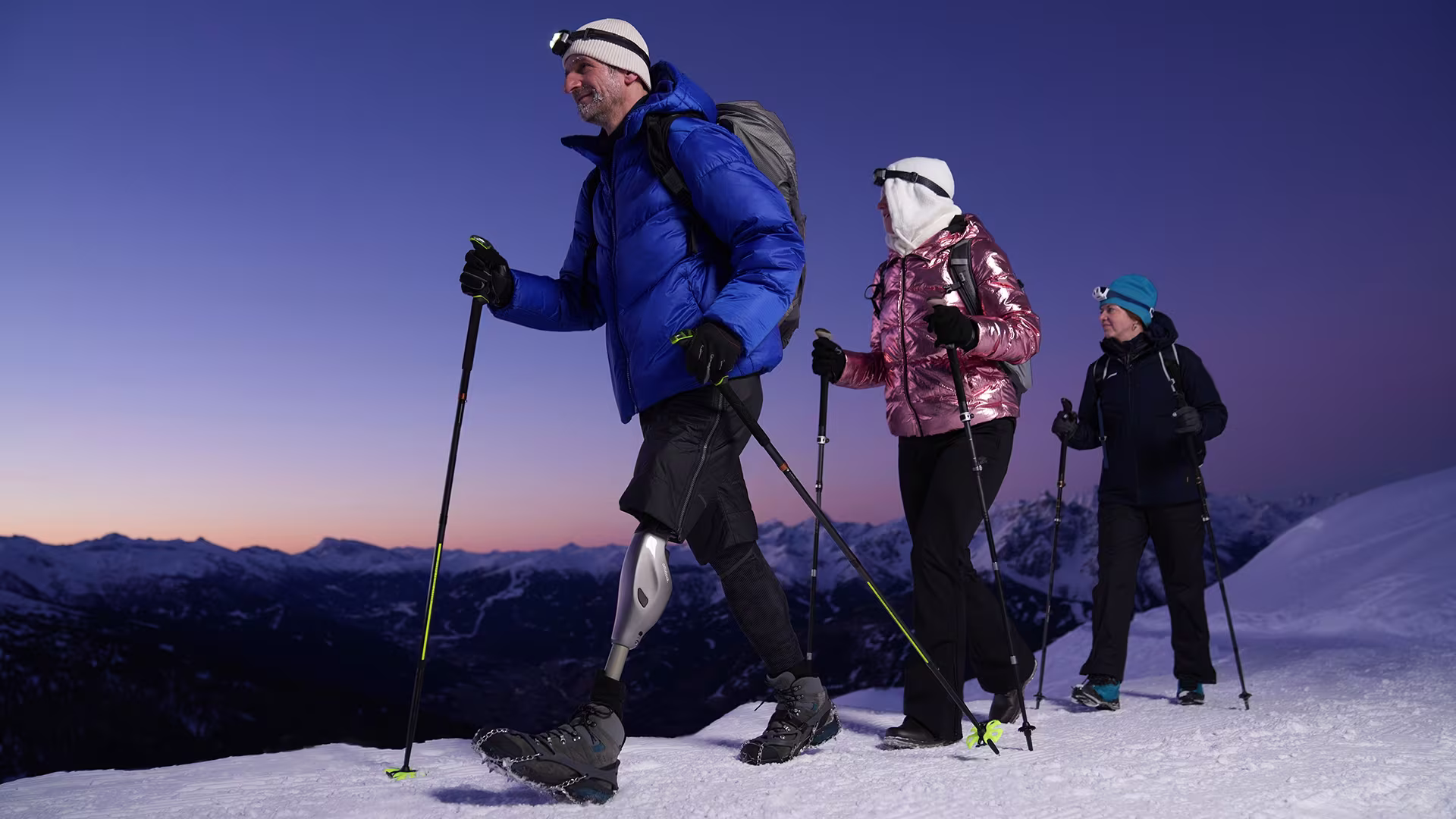 Prosthetic leg user hiking on a snowy mountain at night together with other hikers.