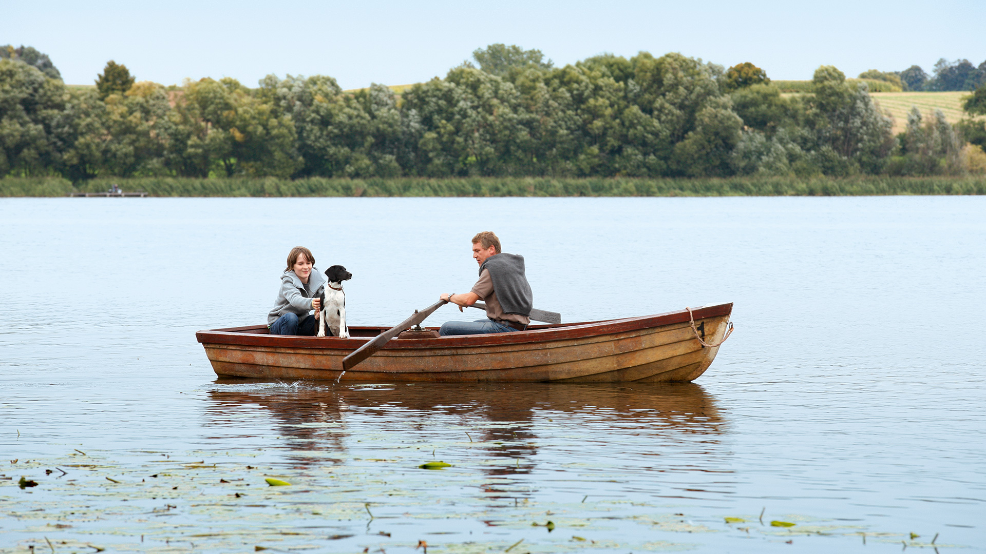 Two people and their dog rowing a boat in a lake