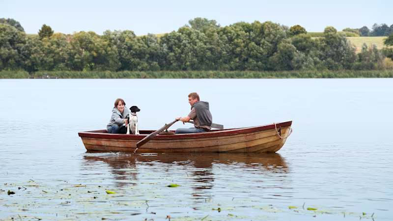 Two people and their dog rowing a boat in a lake