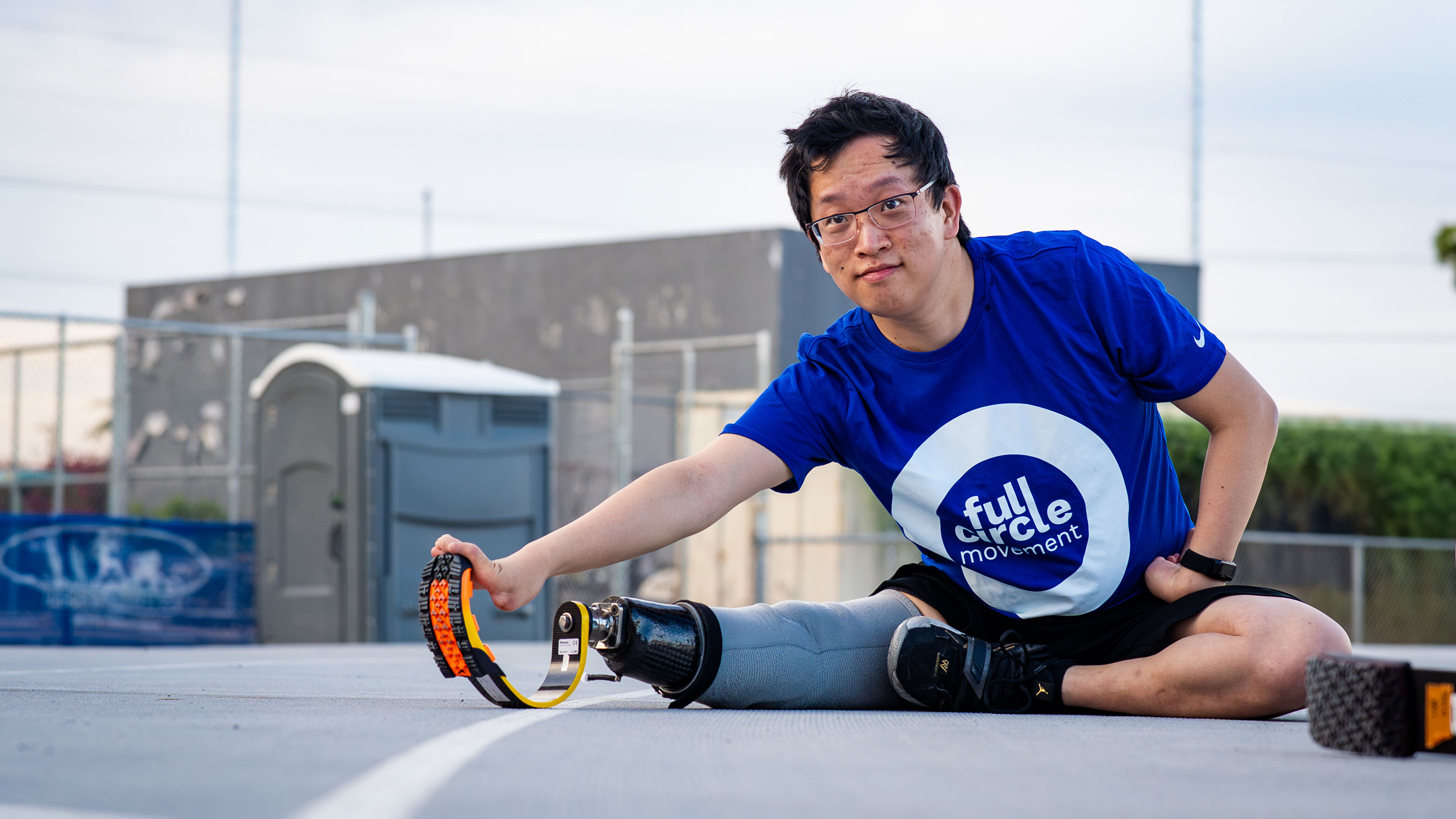 An running prosthetic leg user stretching on a field to warm up for Full Circle Movement activities