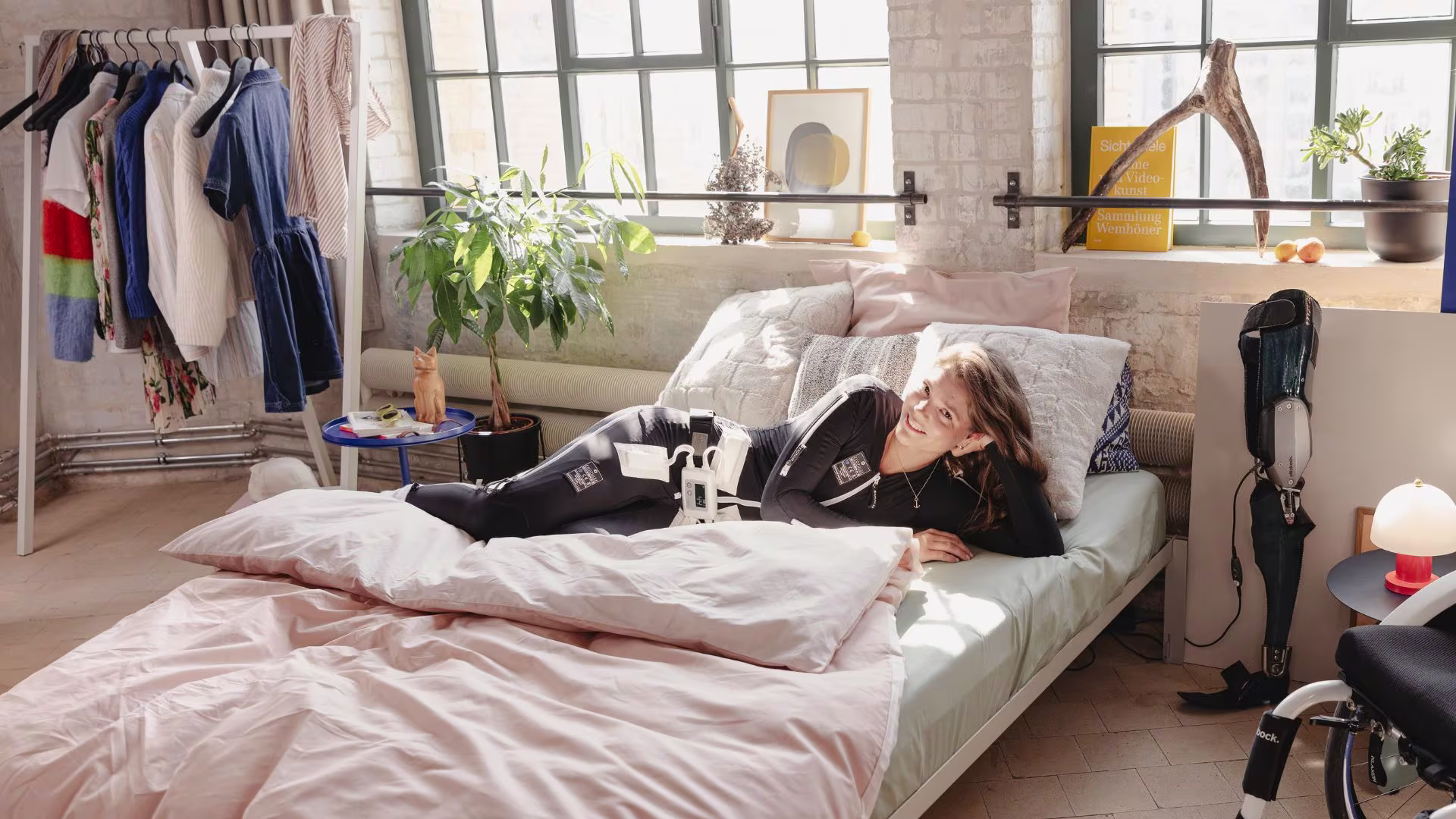 Sina is wearing the Exopulse Mollii Suit and lying on her bed.