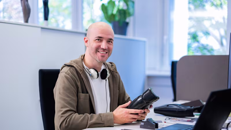Auf dem Bild sieht man einen Ingenieur, der bei Ottobock arbeitet. Er hält einen Teil einer Prothese in der Hand und lächelt in die Kamera.