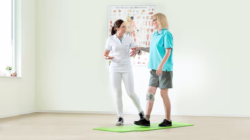 Bir fizyoterapist, klinik ortamında denge egzersizi sırasında Ottobock L300 Go giyen bir kadına yardımcı oluyor.