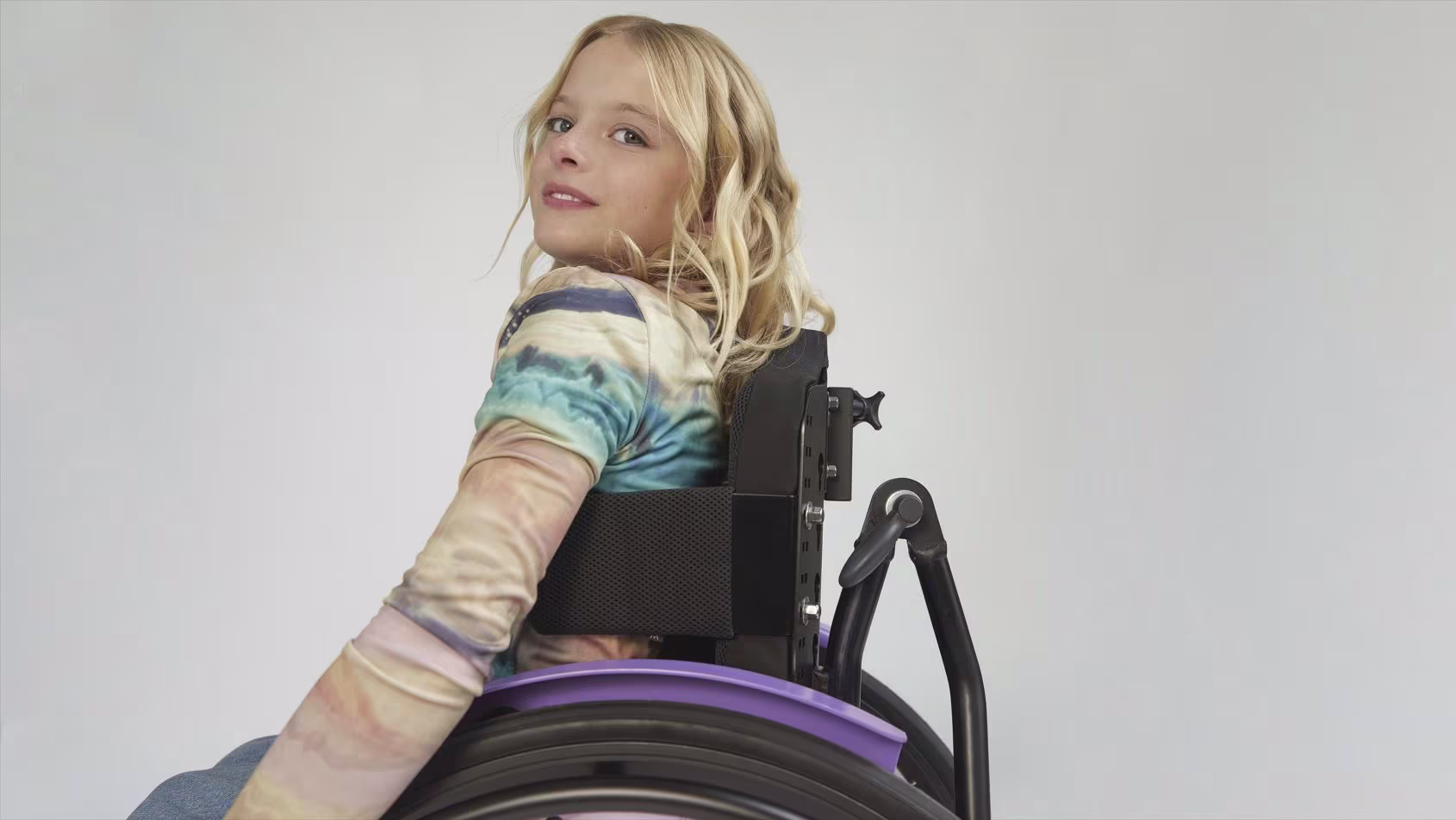Side view with focus on the seat of the Ottobock Kidevo children's wheelchair in which a blonde girl is sitting.
