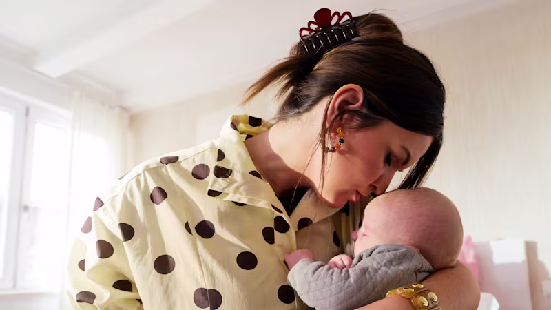 A female prosthesis user is holding her baby in her arms and kissing it on the forehead.