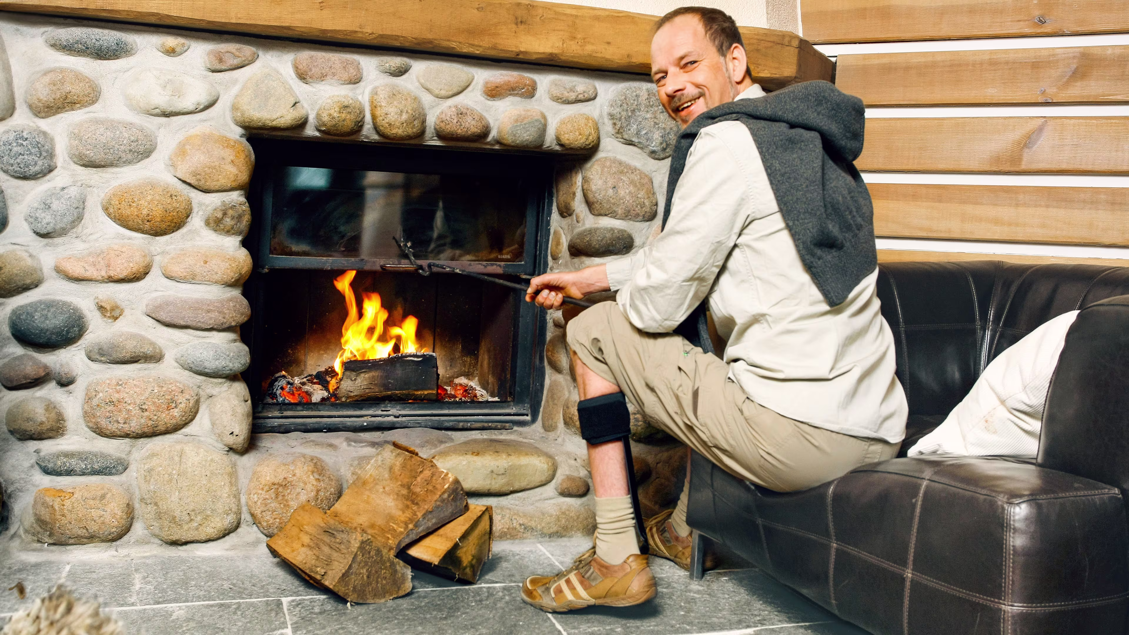 Man with orthosis sits by the fireplace.