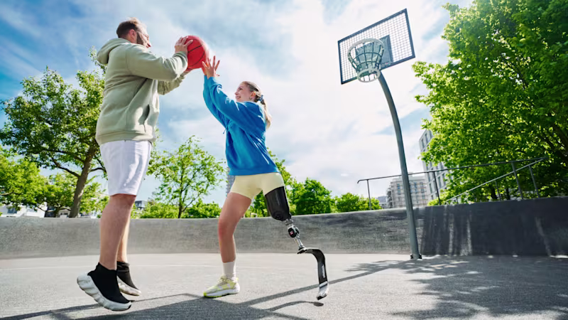 Two people playing basketball, one wearing a prosthetic running blade