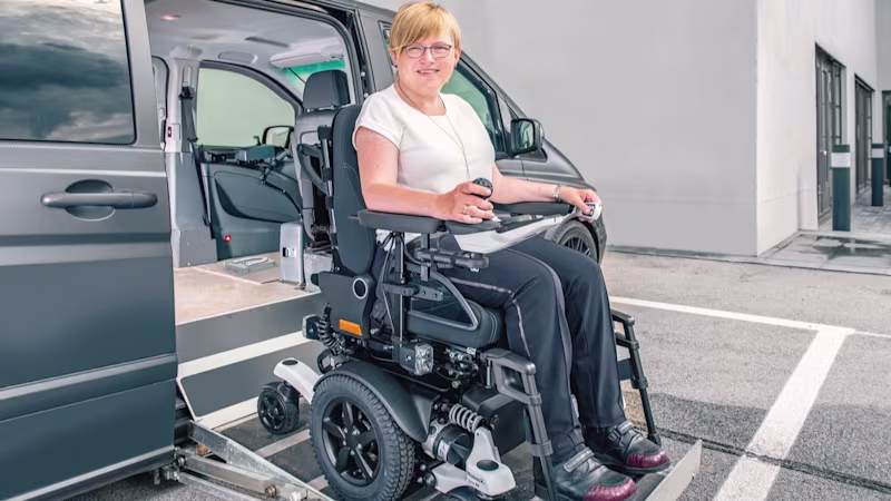 A woman in an Ottobock Juvo power wheelchair drives out of a van via a ramp.