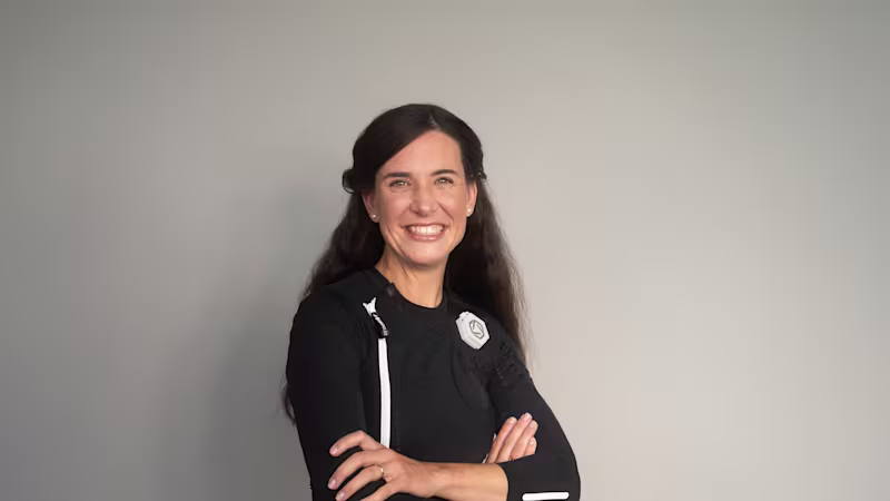 Eine dunkelhaarige Frau trägt den exopulse suit von Ottobock. Sie sitzt auf einem beigen Sofa und lächelt in die Kamera.