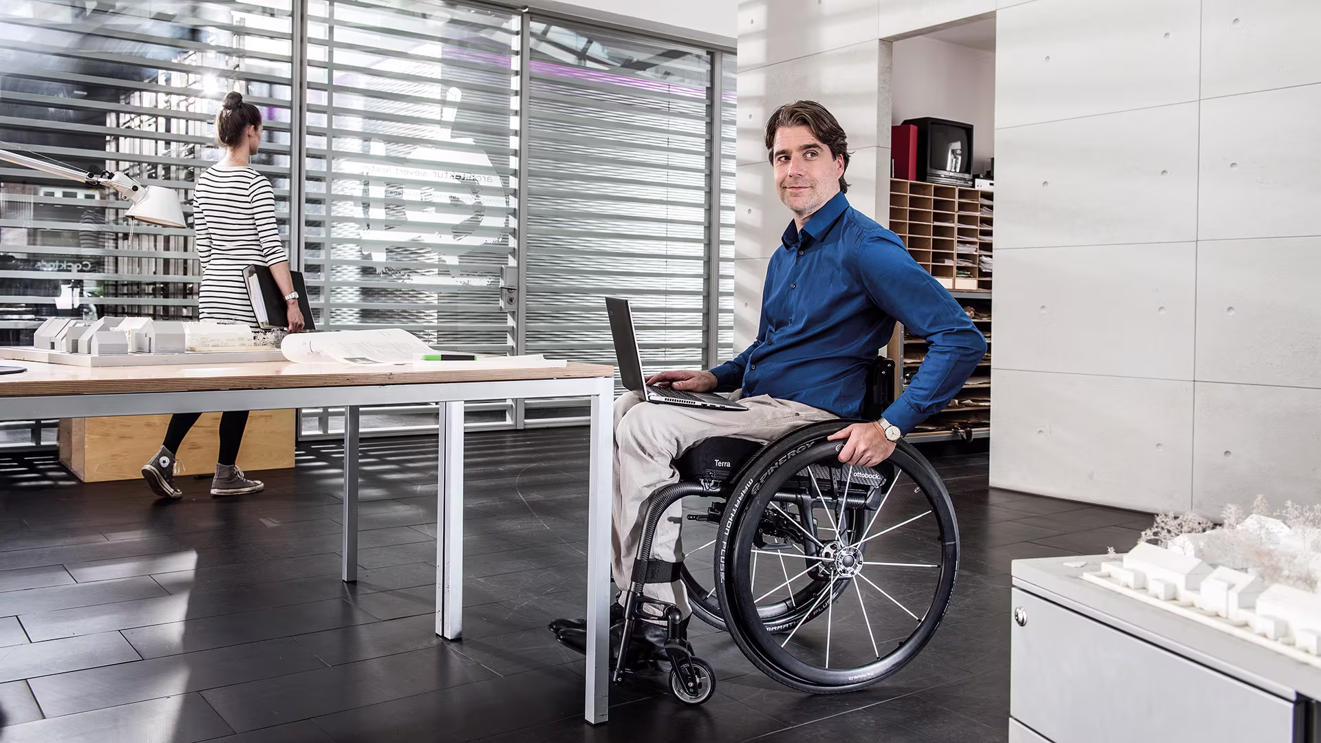 A man in his Zenit manual wheelchair from Ottobock is sitting in with a laptop on his la next to a desk in an office. 