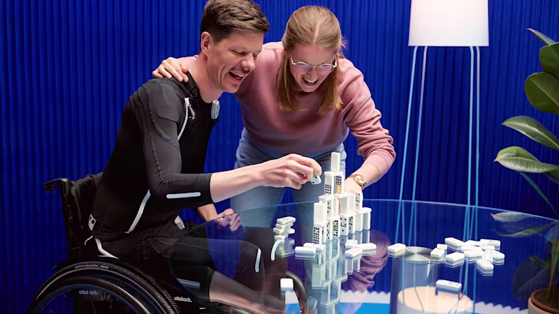 Ottobock exopulse user in front of a blue background picking up Domino pieces