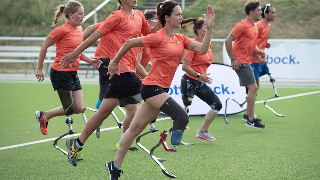 A group of adaptive athletes running on a grass field in running prosthetics by Ottobock