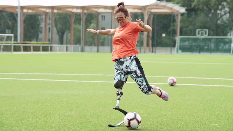 An amputee kicks a football on an outdoor field