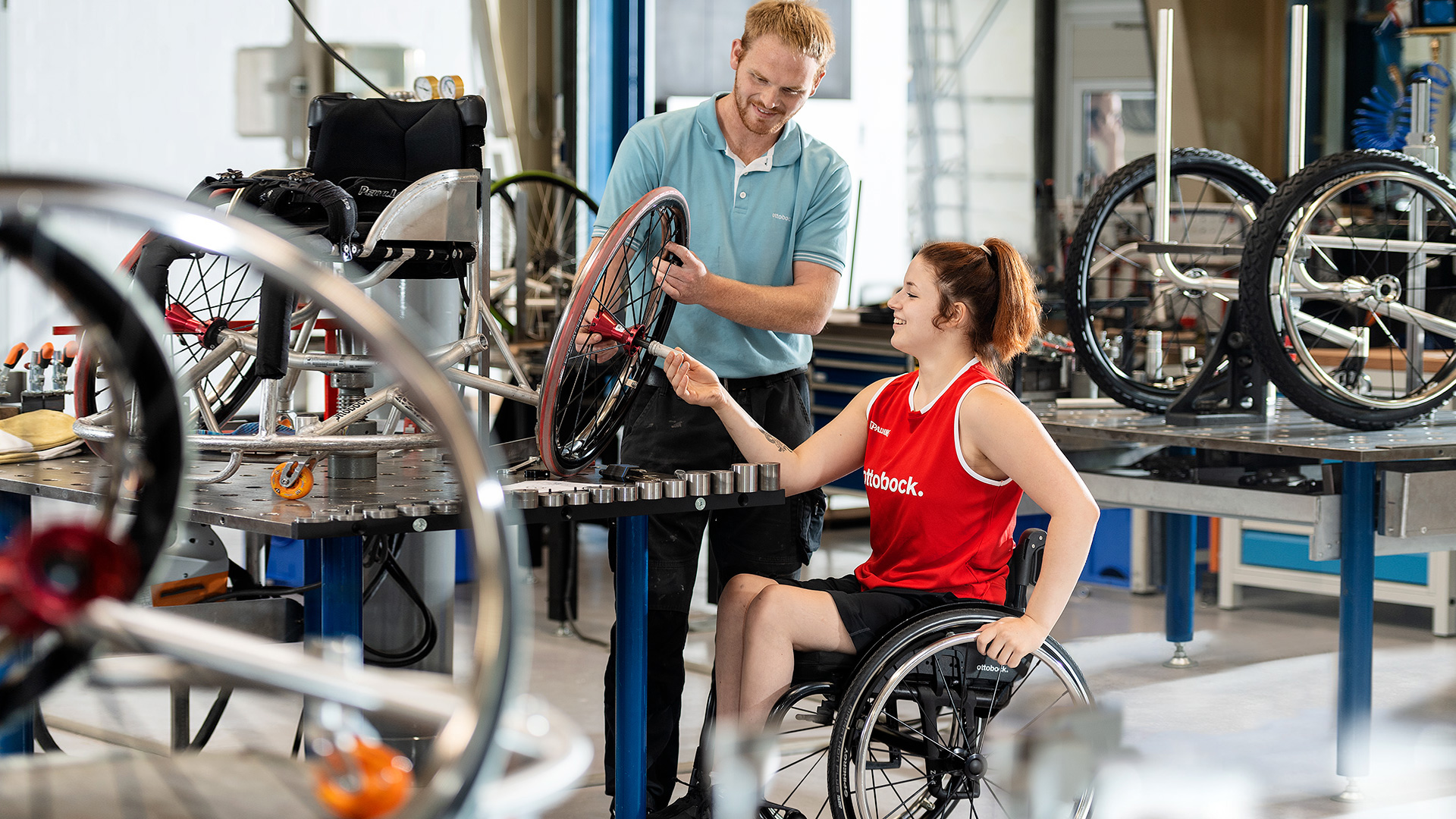 An Ottobock employee is in the workshop together with a sports wheelchair user, adjusting her sports wheelchair.