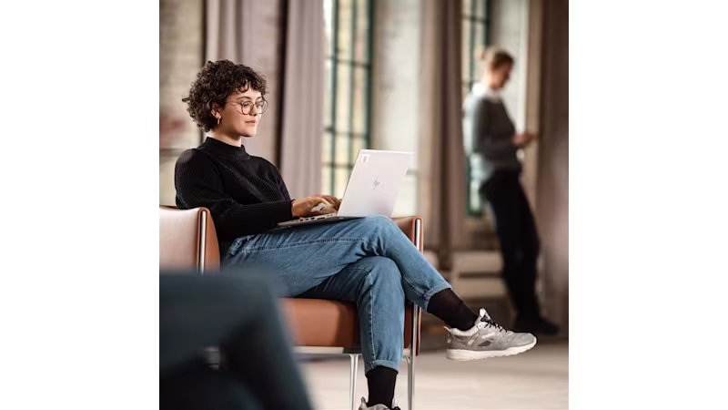 Ottobock prosthetic hand user seated in a chair working comfortable on her laptop.