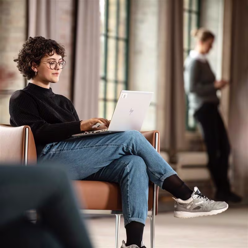 Ottobock prosthetic hand user seated in a chair working comfortable on her laptop.