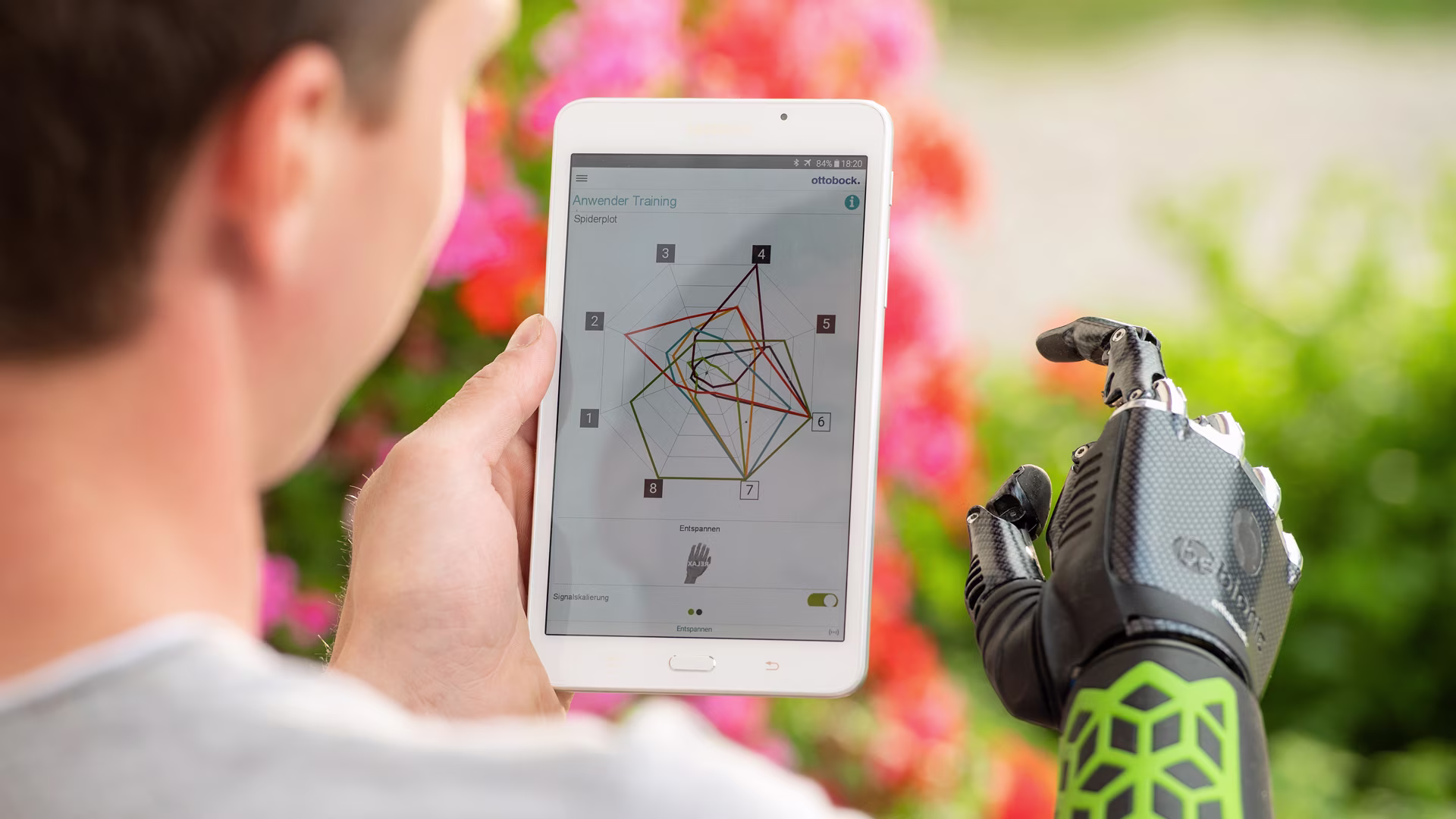 Nahaufnahme eines Mannes, der in der linken Hand ein Tablet hält. Auf diesem ist die Steuerung für seine Myo Plus Armprothese geöffnet, mit der er die Armprothese trainieren kann