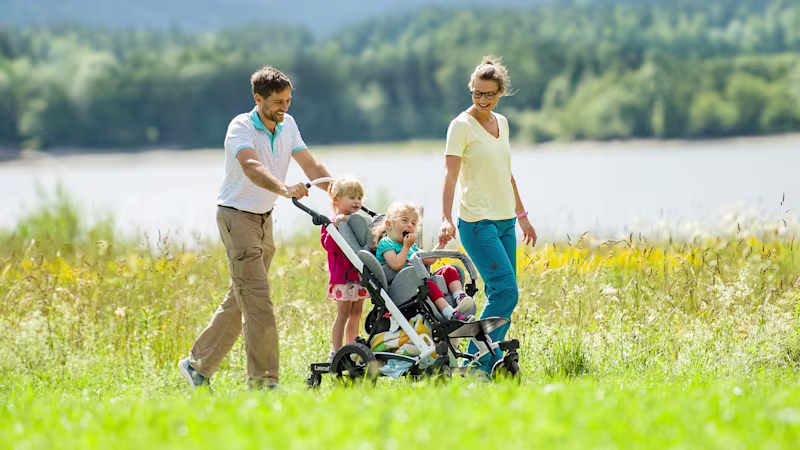 Emilia is sitting in her Ottobock Kimba buggy and being pushed by her father. The family is taking a walk by a lake.