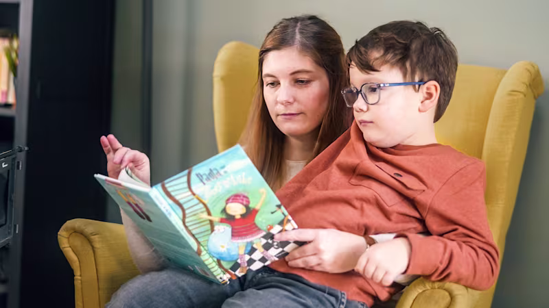 Justus and his mother sitting in a rocking chair while they read a children's book