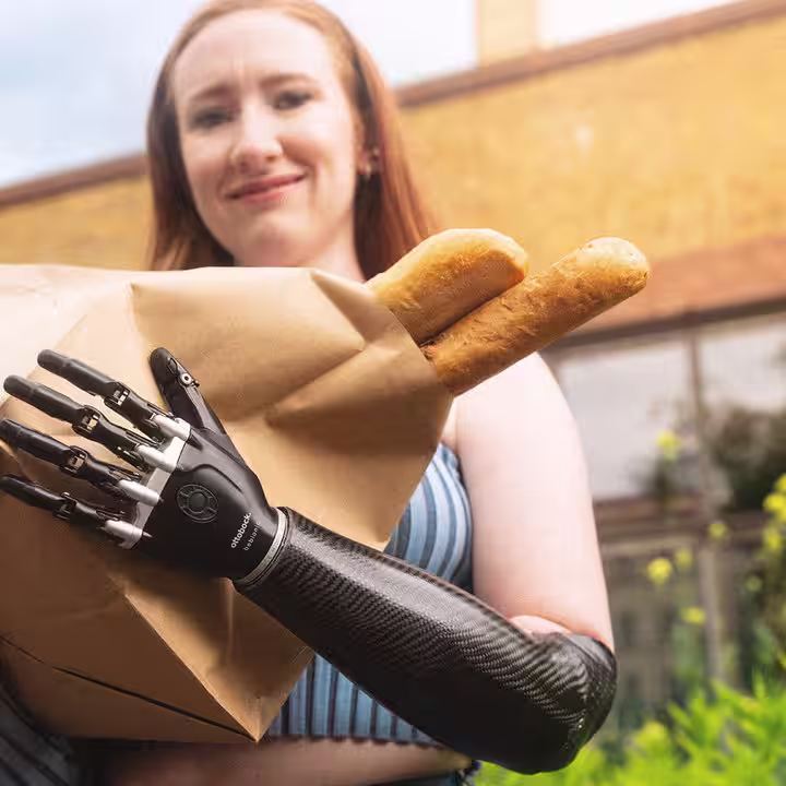 Eine Armprothesenträgerin hält eine Tüte mit Baguette in der Hand. Sie trägt die bebionic Hand von Ottobock.