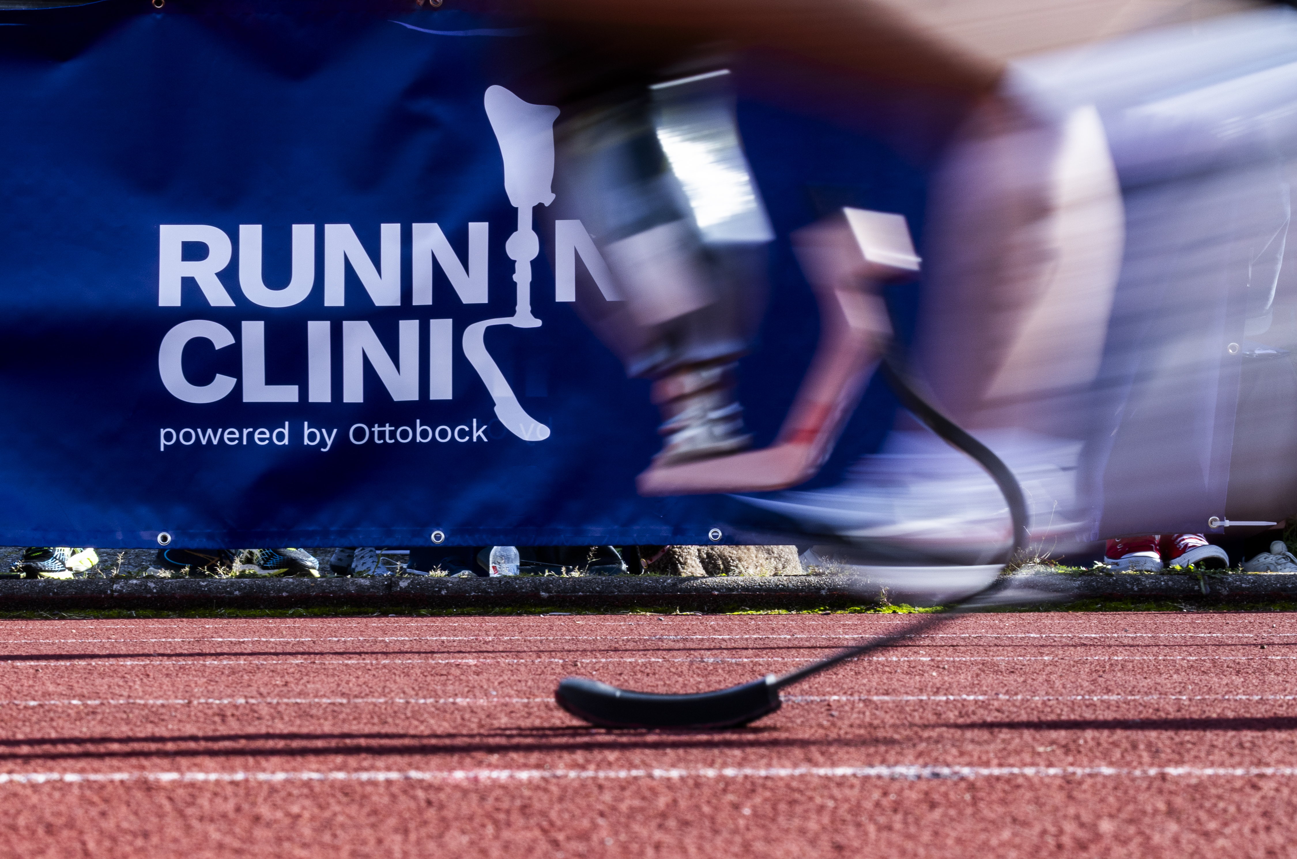 Runner with prosthetic blade passing Running Clinic powered by Ottobock banner on track