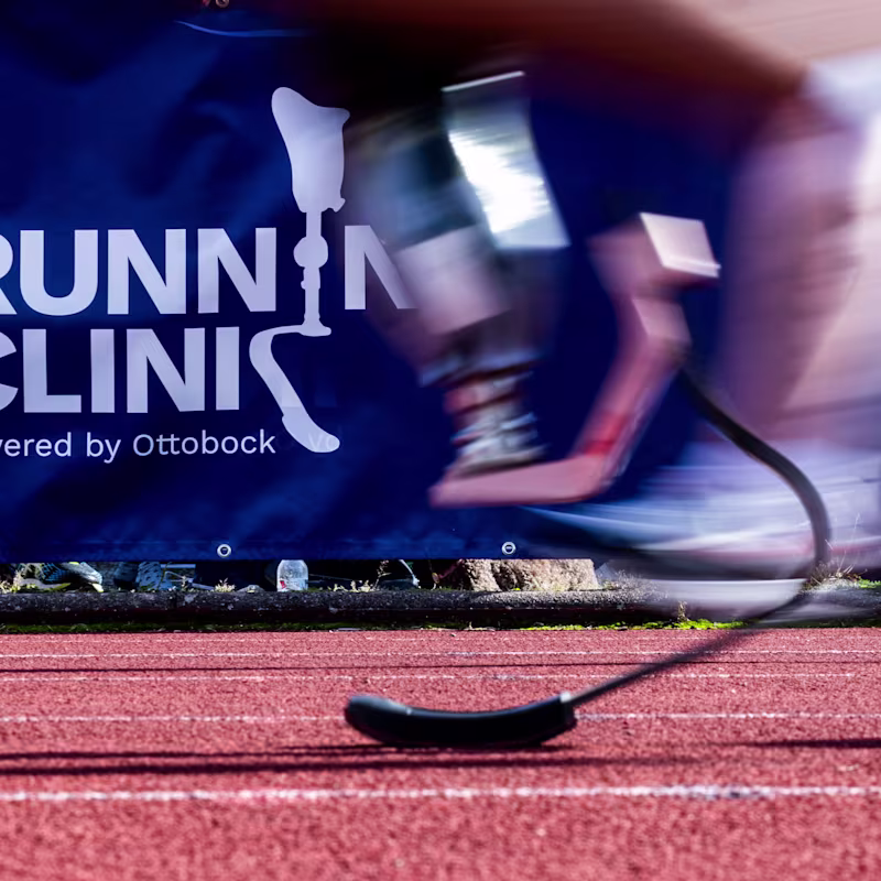Runner with prosthetic blade passing Running Clinic powered by Ottobock banner on track