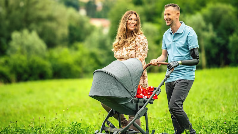 Ein Armprothesenträger spaziert mit seiner Frau und seinem Kind in einem Kinderwagen. Er trägt das DynamicArm-Ellbogengelenk und die bebionic Hand von Ottobock.